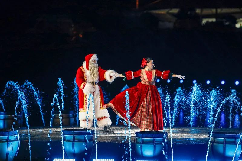 Papai Noel e uma bailarina no palco, com fontes azuis